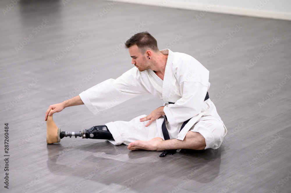 Man with a prosthetic leg stretching in a martial arts studio, demonstrating mobility and balance guided by a skilled prosthetist