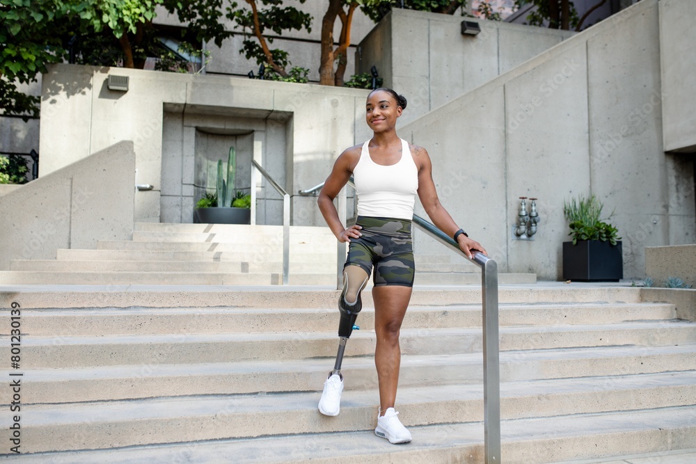 Smiling woman with a prosthetic leg standing on stairs in activewear outdoors

