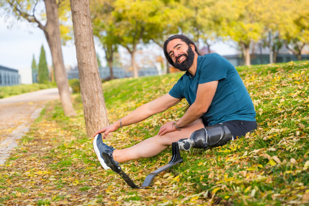 Happy man with a prosthetic leg stretching in a park, showing support for amputees