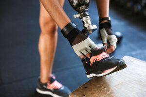 Athlete tightening her shoe while using a lower-limb custom prosthetic leg at the gym.